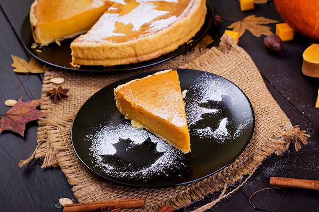 Amerikanischer selbst gemachter Kürbiskuchen mit Zimt und Muskatnuss, Kürbiskernen und Herbstlaub auf einem Holztisch. Thanksgiving-Essen.