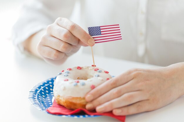 amerikanischer unabhängigkeitstag, feier, patriotismus und feiertagskonzept - nahaufnahme weiblicher hände, die glasierten donut mit amerikanischer flaggendekoration auf einwegteller bei der party am 4. juli von oben dekorieren