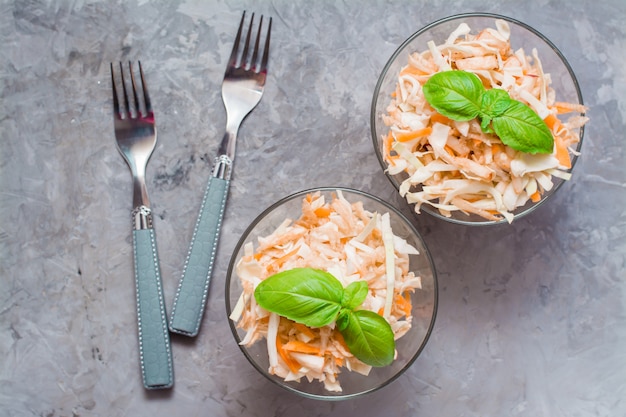 Amerikanischer verzehrfertiger Krautsalat-Salat aus Kohl, Sellerie, Karotten und Äpfeln mit Basilikumblättern in Glasschalen in den Zutaten zum Kochen auf dem Tisch. Das Konzept einer gesunden und richtigen Ernährung.
