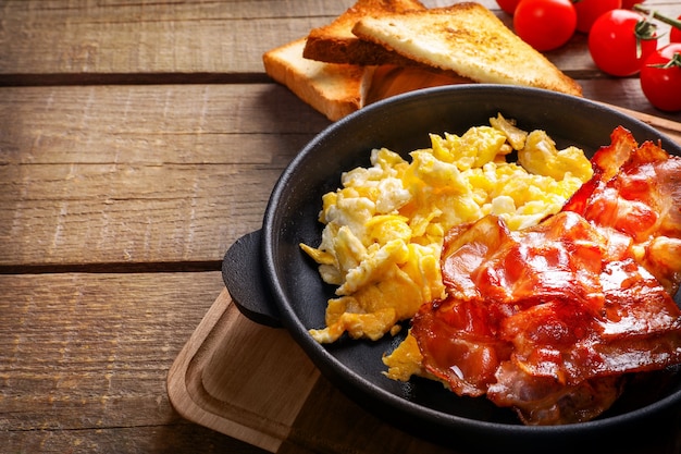 Amerikanisches Frühstück mit Rührei und geröstetem Speck auf Holz.