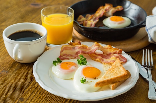 Amerikanisches Frühstück mit Spiegeleiern, Speck, Toast, Pfannkuchen, Kaffee und Saft