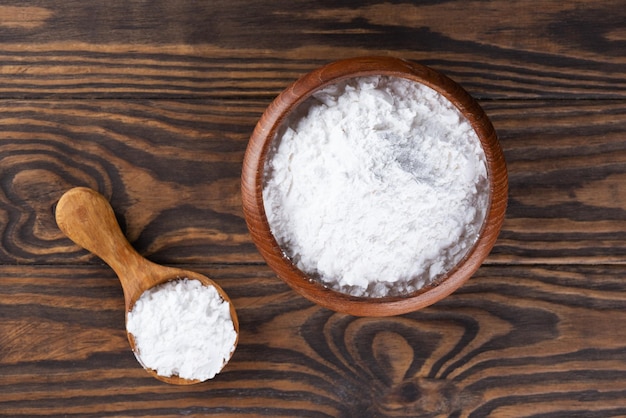 Foto amido de tapioca em uma colher de pau marrom e raiz de mandioca seca em uma mesa de madeira