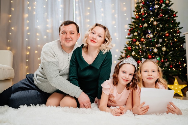 Una amigable familia feliz escribe una carta a santa claus en el árbol de navidad