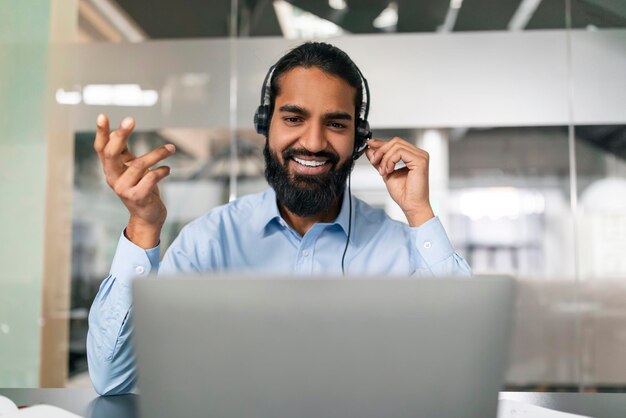 Amigable hombre indio empleado de oficina con auriculares haciendo una llamada web