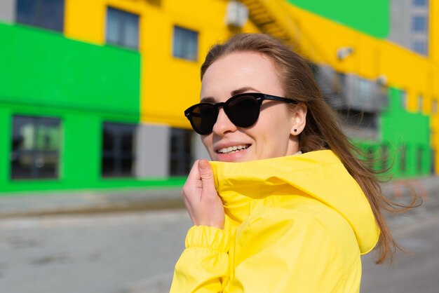 Una amigable joven con una chaqueta amarilla y gafas de sol en la calle