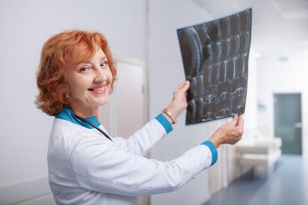 Amigable oncóloga sonriendo a la cámara, sosteniendo una resonancia magnética de un paciente