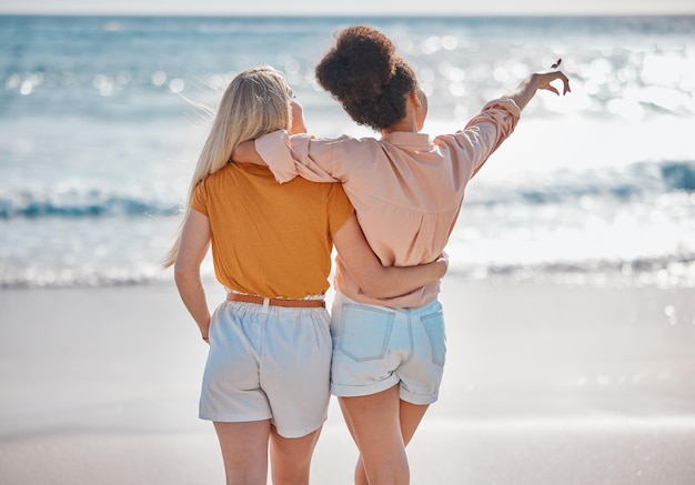 Amigas y abrazos para relajarse en la playa para viajes de vacaciones de verano o viajar juntas al aire libre Mujeres interraciales abrazándose y disfrutando de viajes o aventuras por la costa del océano