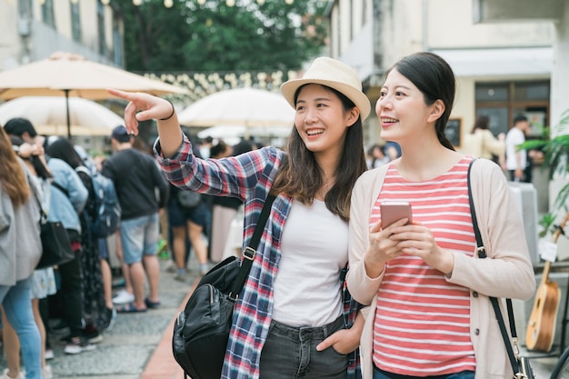 amigas asiáticas no mercado do fazendeiro ao ar livre no verão na cidade. duas jovens viajantes femininas segurando o celular com o aplicativo on-line do mapa pesquisando e apontando o dedo enquanto encontram o destino da loja tóquio japão