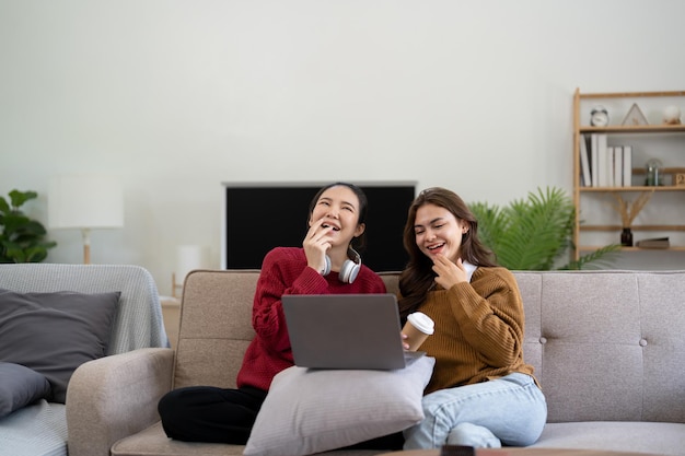 Amigas asiáticas sentadas na sala assistindo filme no laptop juntas Amizade feminina moderna desfruta de estilo de vida de atividade de fim de semana com tecnologia sem fio em casa