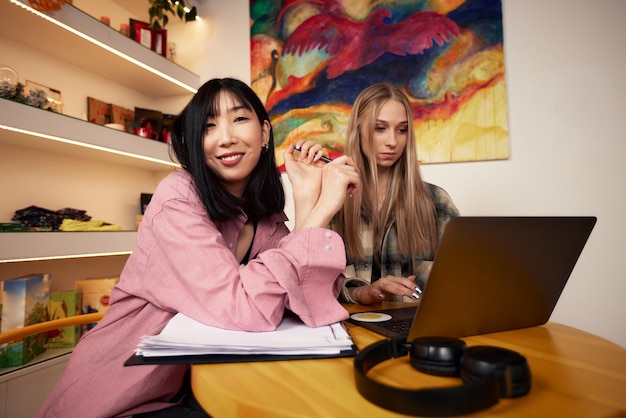 Amigas bailando y escuchando música desde una computadora portátil en casa, niñas divirtiéndose en el apartamento