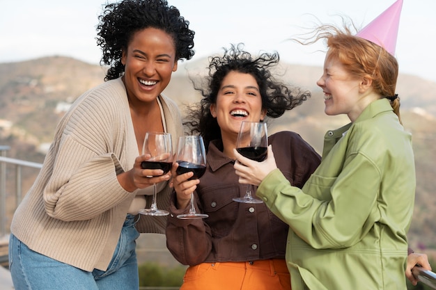 Amigas bebiendo vino y posando durante la fiesta al aire libre