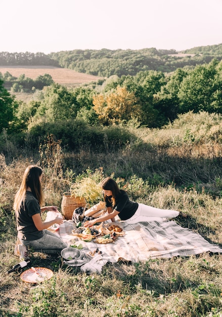 Amigas bonitas das raparigas em um piquenique em um dia de verão. conceito de lazer, férias, turismo