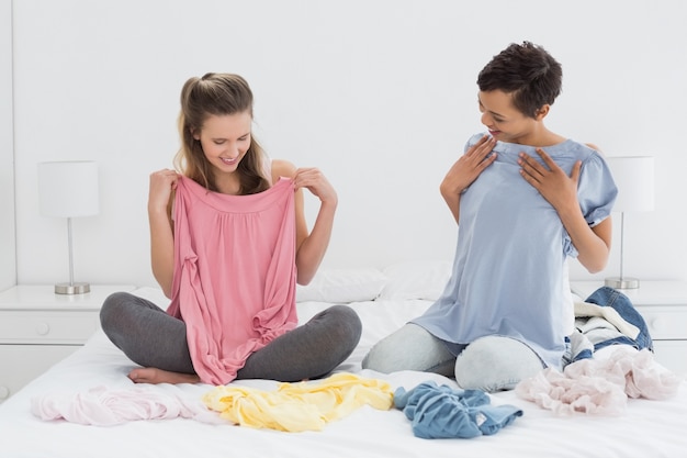 Amigas bonitas que seleccionan la ropa en la cama