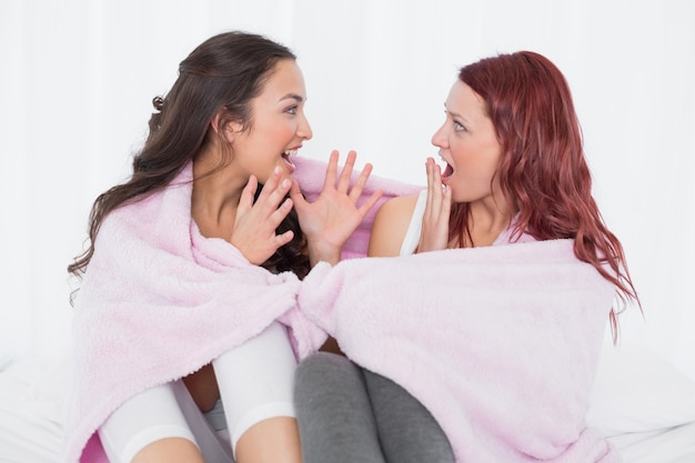 Amigas cubiertas en hoja mientras charlan en la cama