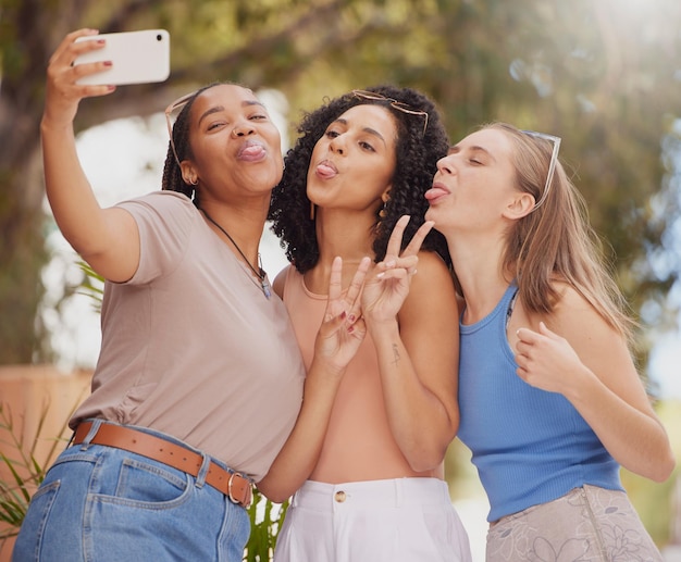 Amigas de selfie e sinal de paz de estudantes junto com viagens e liberdade com diversidade Felicidade feminina e férias de verão felizes tirando uma foto de perfil de mídia social no parque de férias