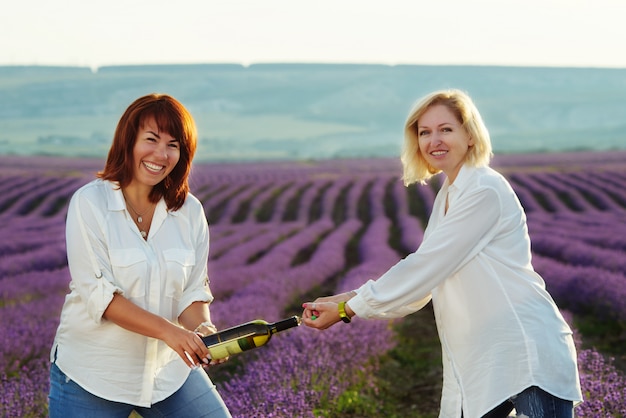 Foto amigas divertidas con botella de vino en campo lavanda