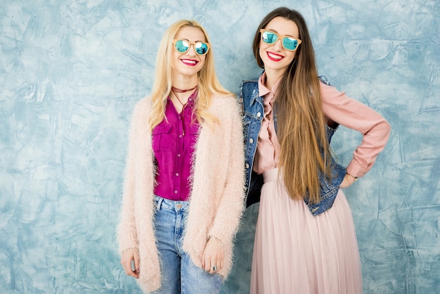 Amigas con estilo divirtiéndose juntos en el fondo de la pared azul