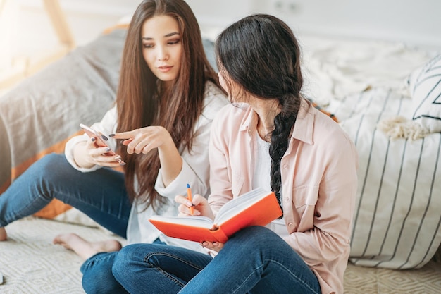 Amigas estudando sentadas na cama em casa.
