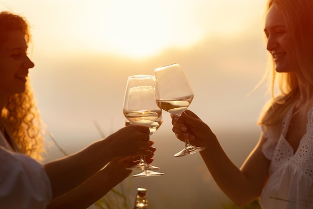 Amigas fazem um brinde com copos de vinho branco no pôr-do-sol.