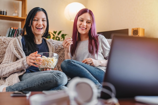 Amigas felices viendo un programa o una película en la computadora portátil en casa