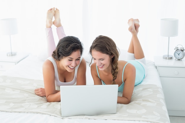 Amigas felizes e relaxadas usando laptop na cama