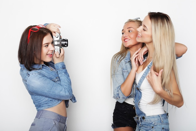 Amigas felizes tomando algunas fotos con la cámara, sobre una pared blanca