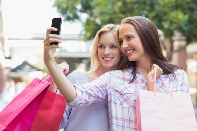 Foto amigas felizes tomando um selfie e segurando sacolas de compras