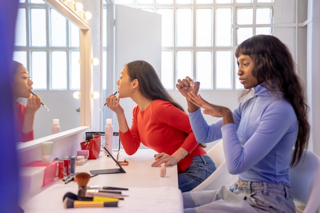 Foto amigas jóvenes poniéndose un poco de maquillaje profesional en el camerino