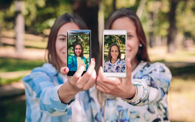 Amigas mostrando teléfonos inteligentes con sus fotos selfie tomadas sobre un bosque