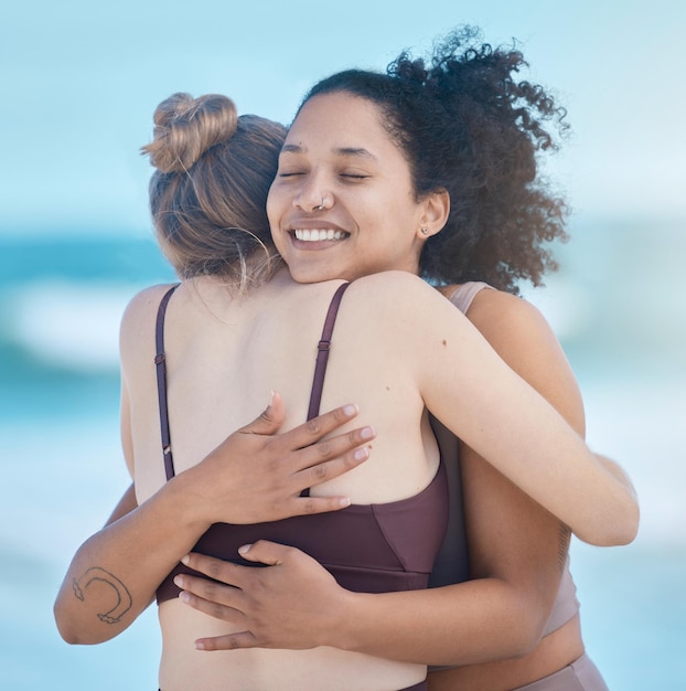 Amigas mulheres e abraços após o exercício ao ar livre, felizes e calmos na praia com amor e fitness juntos Apoie a confiança e a motivação do treino de amizade à beira-mar e bem-estar com sorriso zen