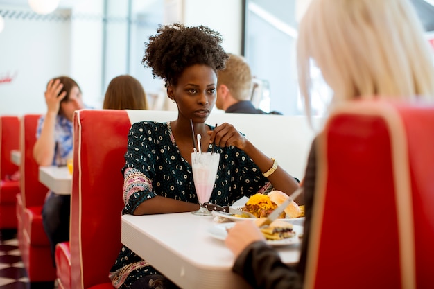 Amigas multirraciales comiendo comida rápida en una mesa en el restaurante