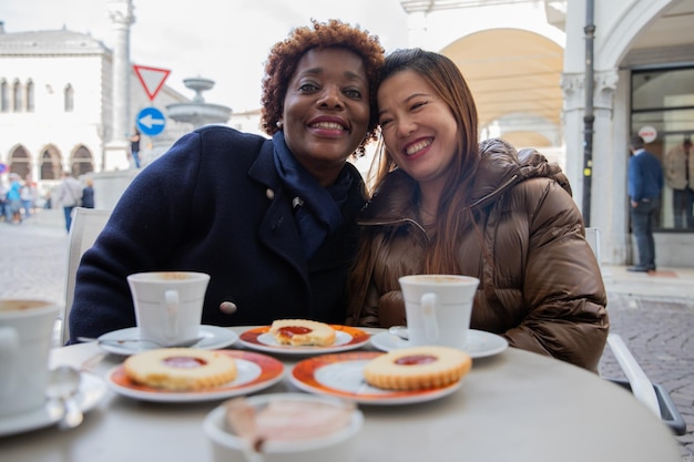 Amigas multirraciales con una gran sonrisa en el bar desayunando