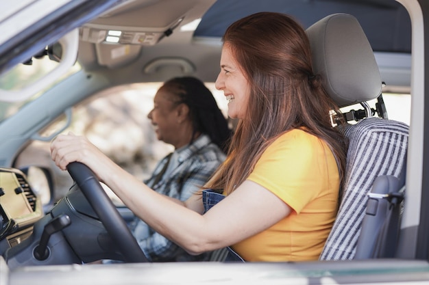 Foto amigas multirraciales maduras divirtiéndose dentro de mini van camper en un viaje por carretera