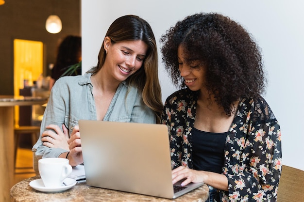Amigas multirraciales sonrientes compartiendo portátiles en una cafetería