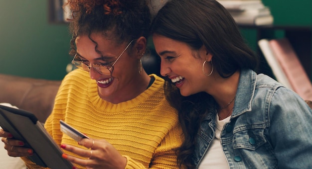 Foto las amigas se ríen y la tarjeta de crédito con la tableta en un sofá de la sala de estar con compras en línea la felicidad de los estudiantes y la mujer joven junto con la compra web y la aplicación de pago de comercio electrónico en un salón de casa