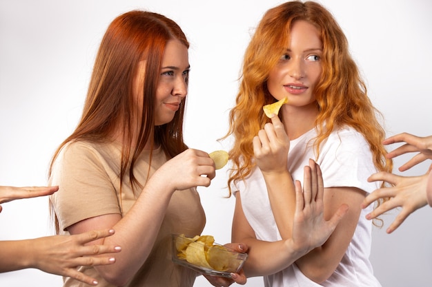 Foto amigas ruivas não querem compartilhar fotos de batatas fritas com muitas mãos para fazer um lanche em uma parede branca