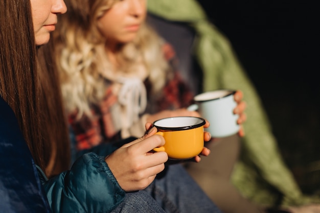 Amigas sentadas em uma barraca tomando chá à noite