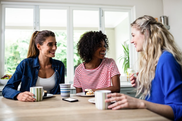 Amigas sonriendo mientras desayunando en la mesa