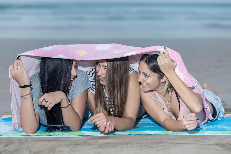 Foto amigas sorridentes em lençóis descansando na praia contra o céu