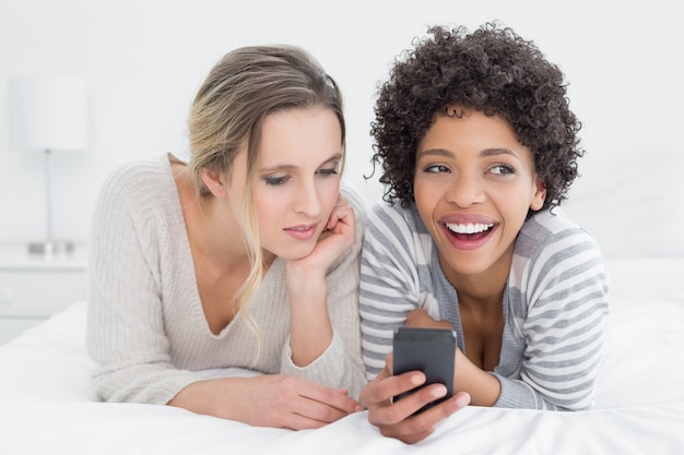 Amigas sorridentes lendo mensagem de texto na cama