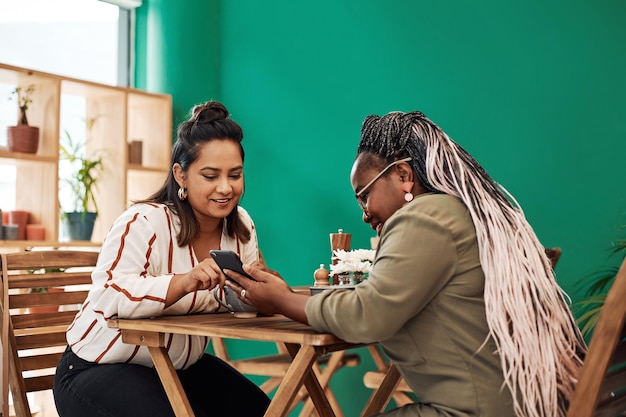 Amigas y teléfonos móviles en cafeterías para redes sociales y conexiones Gente diversidad y feliz con la tecnología para noticias chismes e información o transmisión en cafetería de Nueva York