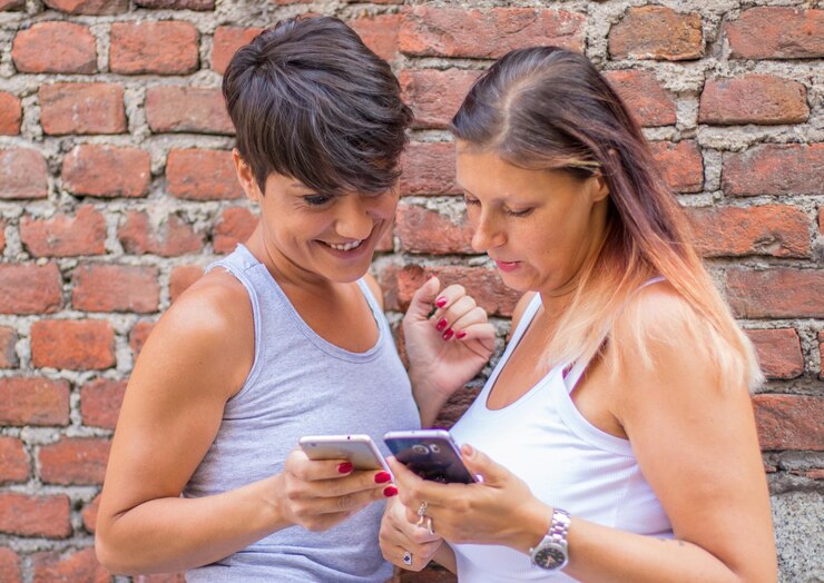 Foto amigas usando teléfonos contra la pared de ladrillo rojo