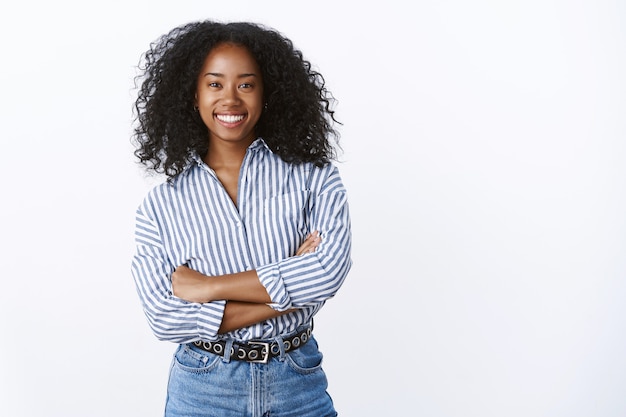 Amigável alegre atraente afro-americana de cabelos encaracolados jovem 25 anos consultora acordando colegas de trabalho, sorrindo agradável, divertindo-se, curtindo o relaxamento da empresa, mãos cruzadas no peito