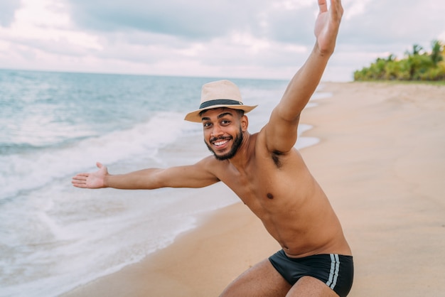 Amigável, confiante e sorridente jovem latino-americano de braços abertos, olhando para a câmera na praia