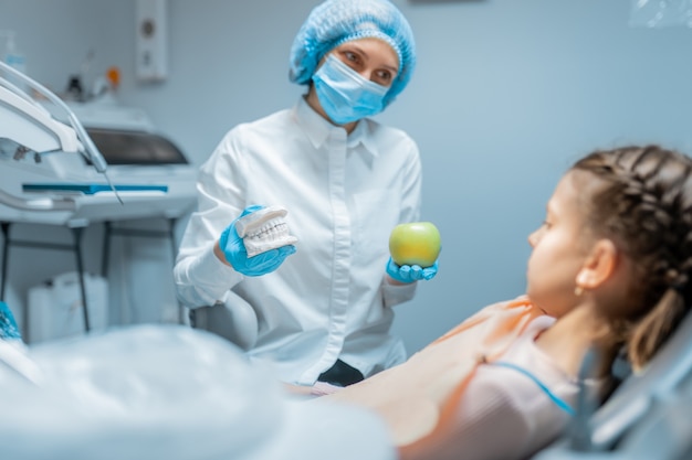 Amigável dentista ortodontista educando a menina paciente usando modelo de dentes e maçã