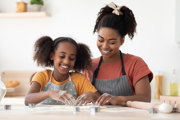 Amigável família negra mãe e filha fazendo diversas figuras com cortadores de biscoito, feliz mãe afro-americana e criança assando juntos em casa, usando figuras de biscoito, conceito de cozimento