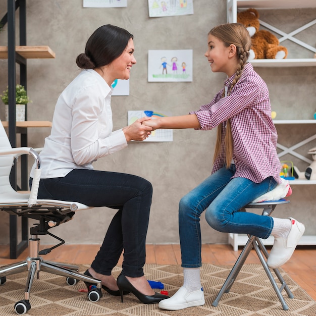 Foto amigável psicólogo feminino segurando as mãos de uma menina na sessão de terapia