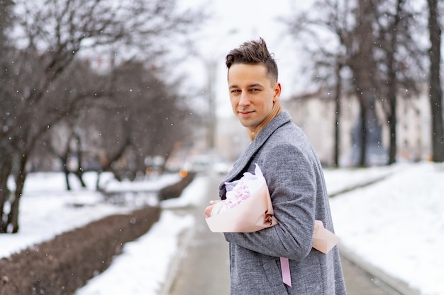 Amigo con un ramo de hortensias de flores rosas esperando a su novia al aire libre mientras cae la nieve. Concepto del día de Valetnine, propuesta de boda. el hombre va a una cita.