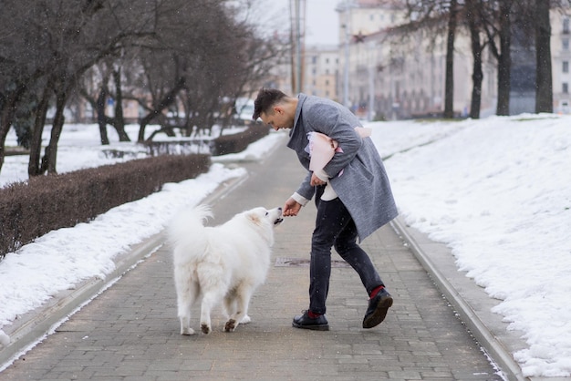 Foto amigo con un ramo de hortensias de flores rosas esperando a su novia y caminando y jugando con un perro. al aire libre mientras cae la nieve. concepto del día de valetnine, propuesta de boda. mangos