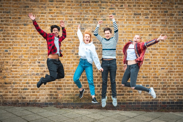 Amigos adolescentes felices saltando delante de una pared